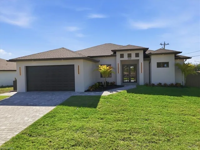 Prairie-style home featuring french doors, decorative driveway, a front yard, an attached garage, and stucco siding
