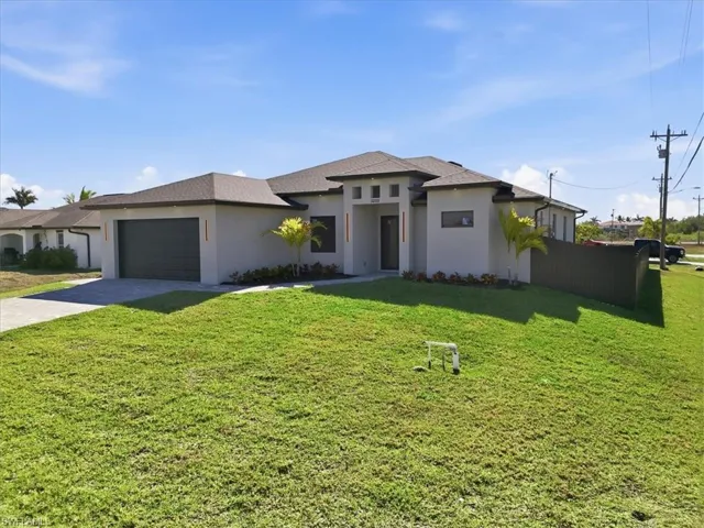Prairie-style home featuring a front lawn, stucco siding, driveway, and a garage