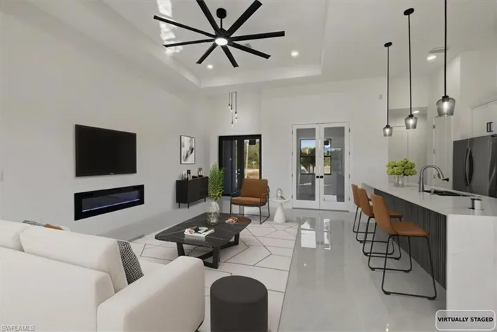 Living area featuring french doors, a high tray ceiling, a ceiling fan, light tile patterned floors, and recessed lighting