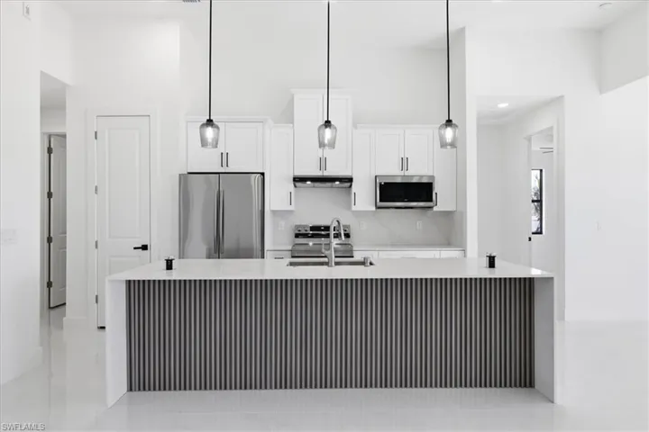 Kitchen featuring light stone counters, stainless steel appliances, an island with sink, white cabinets, and a high ceiling