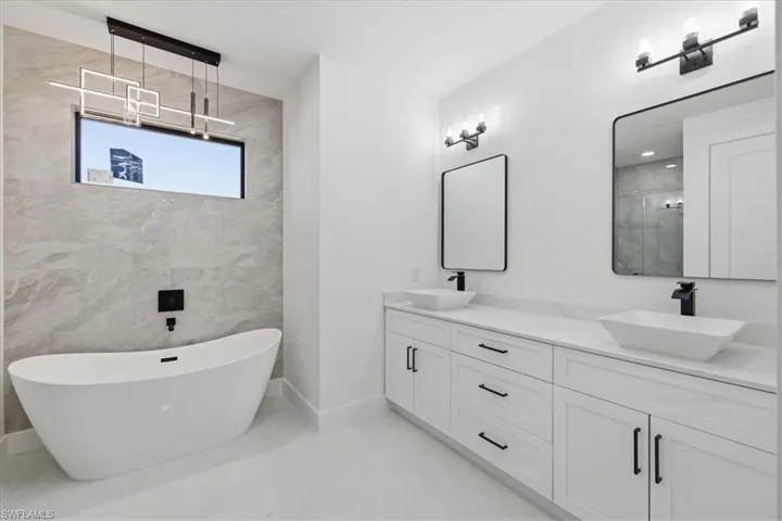 Full bathroom featuring double vanity, a freestanding bath, a walk in shower, and tile walls