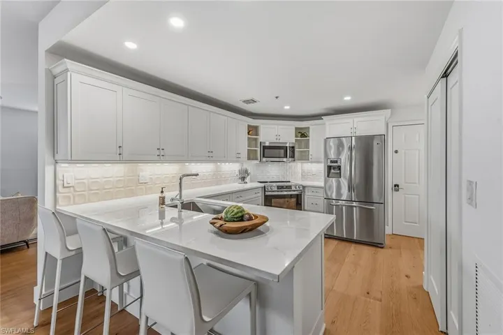 Kitchen featuring appliances with stainless steel finishes, tasteful backsplash, white cabinetry, a breakfast bar, and light wood-style flooring