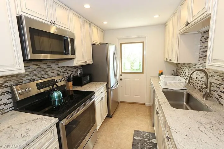 Kitchen with stainless steel appliances, sink, tasteful backsplash, and light stone counters