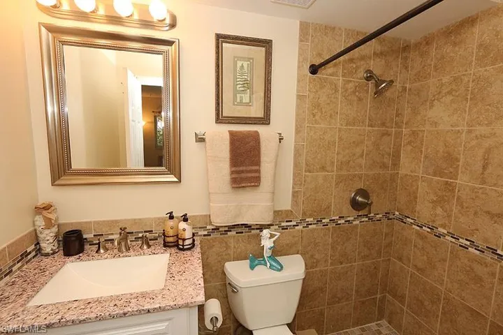 Bathroom with tiled shower, tile walls, toilet, tasteful backsplash, and vanity