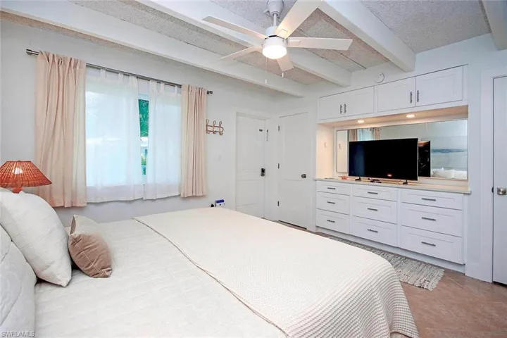 Bedroom featuring beam ceiling, a ceiling fan, light tile patterned floors, and a textured ceiling