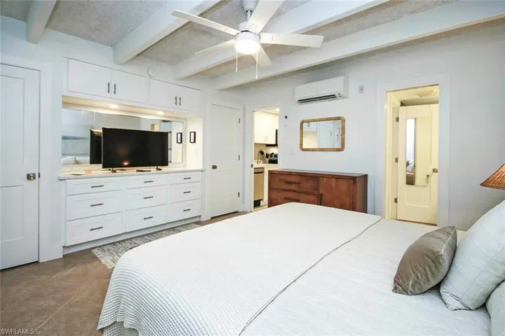 Bedroom featuring beam ceiling, light tile patterned floors, ceiling fan, and a wall mounted AC