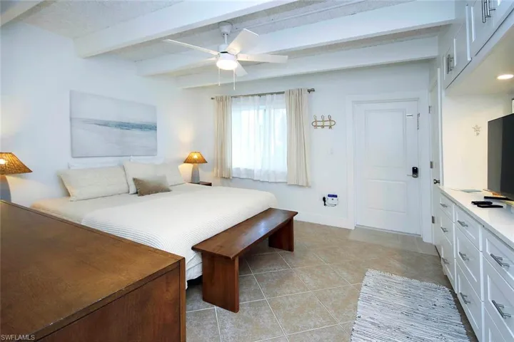 Bedroom with beamed ceiling, light tile patterned floors, and ceiling fan