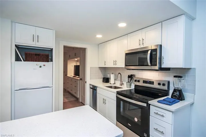 Kitchen with appliances with stainless steel finishes, white cabinetry, tasteful backsplash, light stone countertops, and recessed lighting