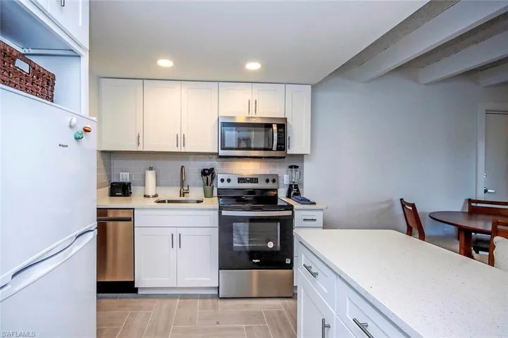Kitchen with white cabinetry, backsplash, stainless steel appliances, light stone counters, and recessed lighting