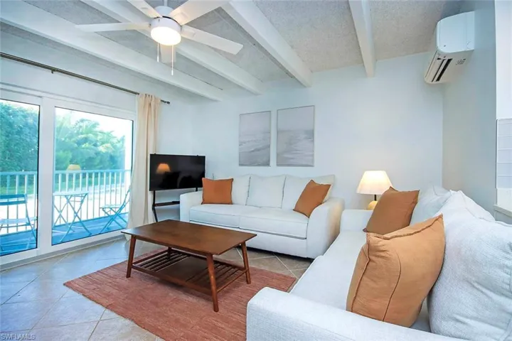 Living area with tile patterned flooring, beam ceiling, an AC wall unit, a ceiling fan, and a textured ceiling
