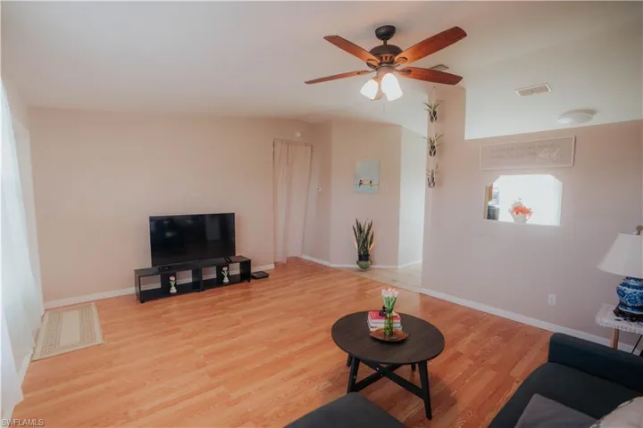 Vaulted ceiling with a ceiling fan, wood-finish flooring, and ample natural light from multiple windows