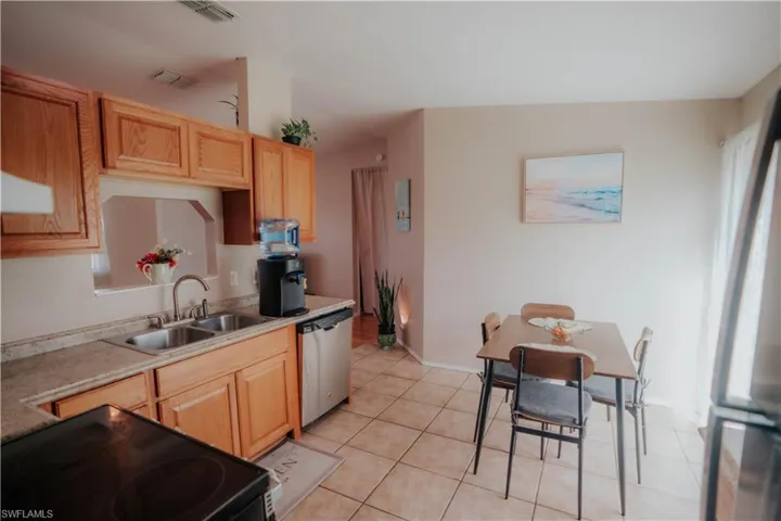 Kitchen featuring wood cabinetry, stainless steel dishwasher, dual basin sink, light-toned countertops, and tiled flooring