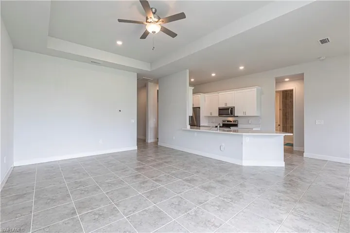 Unfurnished living room with ceiling fan, light tile patterned floors, and a tray ceiling