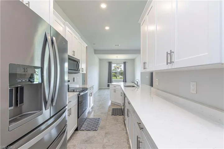 Kitchen with white cabinetry, light stone counters, appliances with stainless steel finishes, and light tile patterned floors