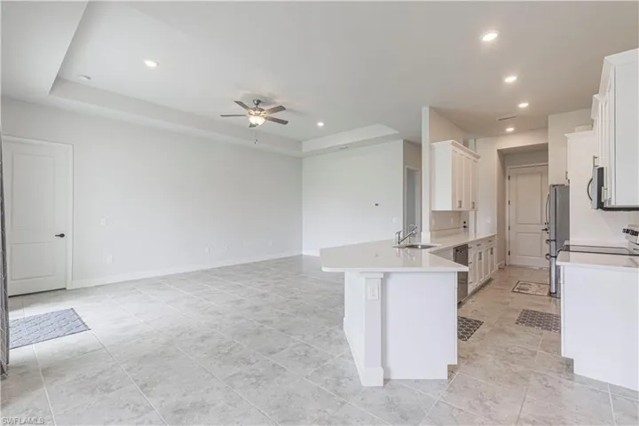 Kitchen with light tile patterned floors, kitchen peninsula, a raised ceiling, and ceiling fan