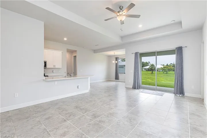 Unfurnished living room with ceiling fan, sink, a tray ceiling, and light tile patterned floors