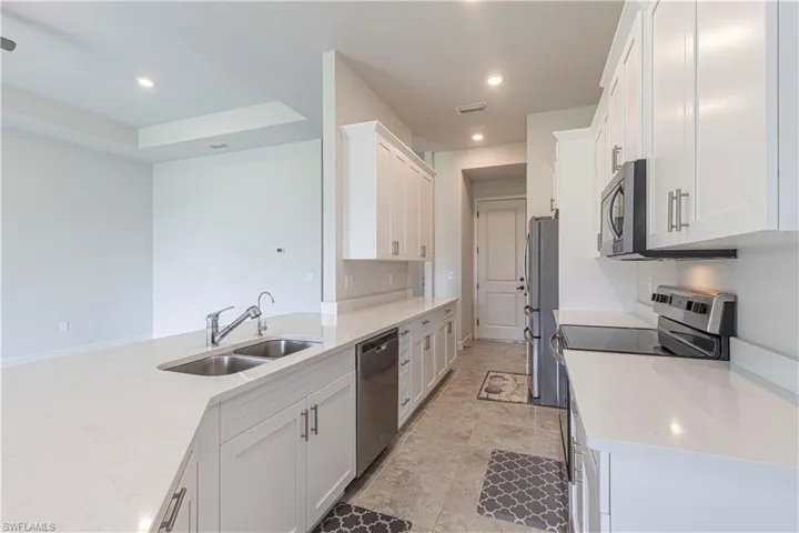 Kitchen with appliances with stainless steel finishes, light tile patterned floors, white cabinets, and sink
