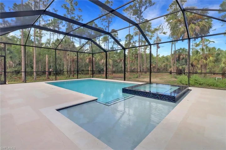 View of swimming pool with glass enclosure, a patio area, and an in ground hot tub