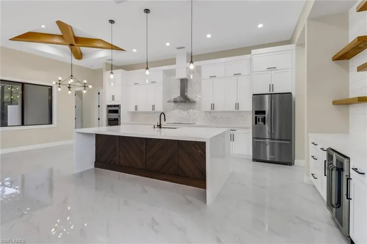 Kitchen with a notable chandelier, tasteful backsplash, stainless steel appliances, a center island with sink, and white cabinets