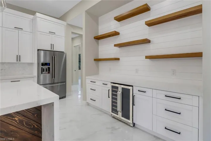 Kitchen featuring wine cooler, light stone countertops, stainless steel fridge with ice dispenser, and white cabinets