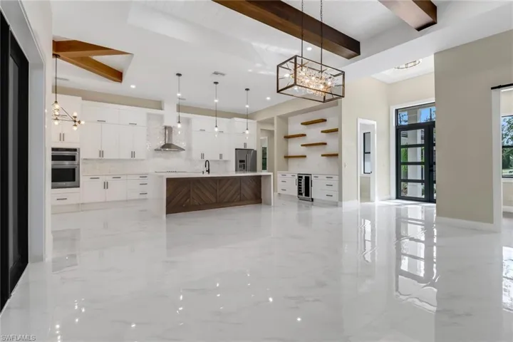 Kitchen with decorative light fixtures, stainless steel appliances, an island with sink, white cabinets, and wall chimney range hood