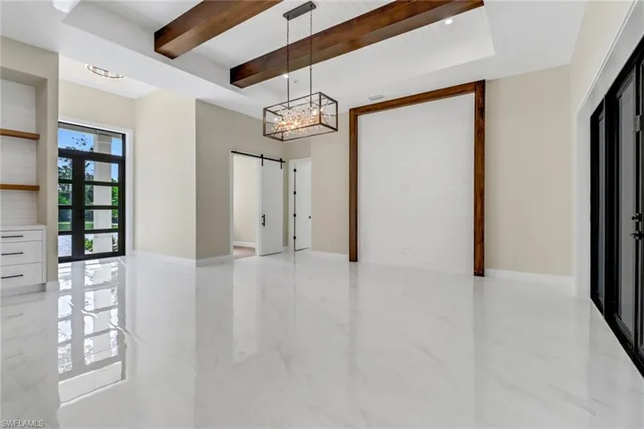 Empty room with a barn door, a notable chandelier, and beam ceiling