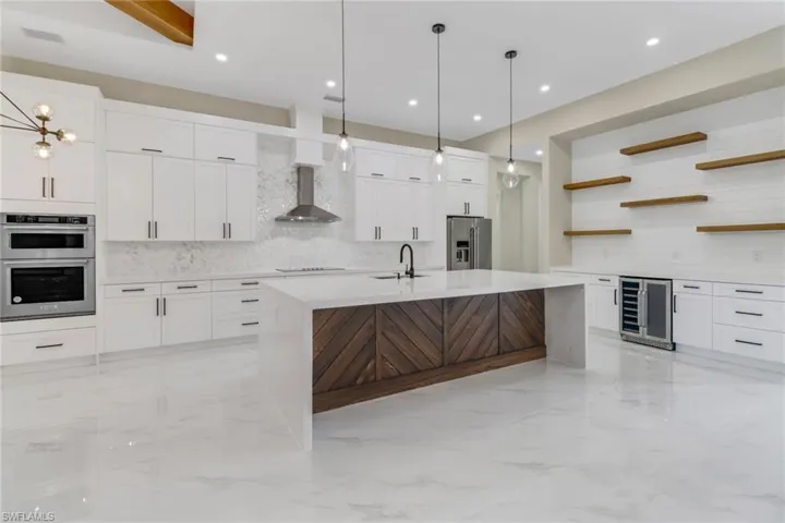 Kitchen with white cabinets, stainless steel appliances, wall chimney exhaust hood, wine cooler, and a kitchen island with sink