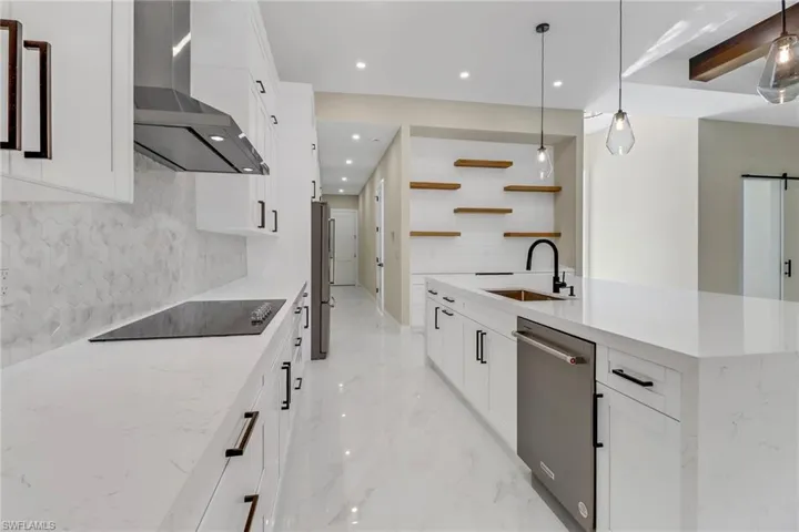 Kitchen featuring a center island with sink, stainless steel appliances, sink, decorative backsplash, and wall chimney range hood