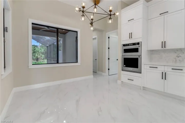 Kitchen featuring decorative light fixtures, white cabinets, a notable chandelier, and stainless steel double oven