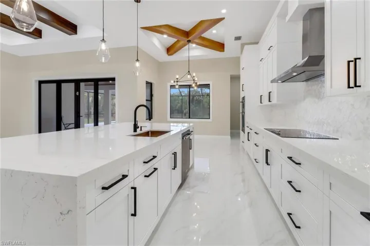 Kitchen featuring wall chimney range hood, light stone counters, sink, black electric cooktop, and a large island