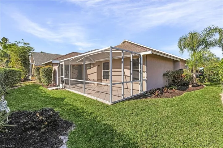 Back of house with a lanai, a patio area, and a lawn