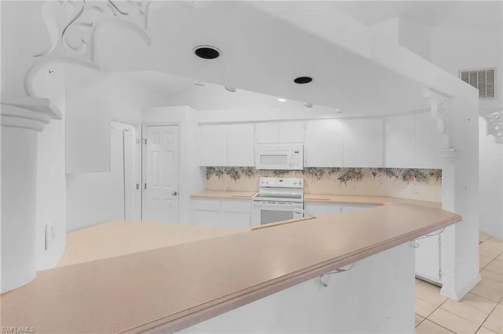 Kitchen featuring white cabinetry, white appliances, decorative backsplash, and light tile patterned floors