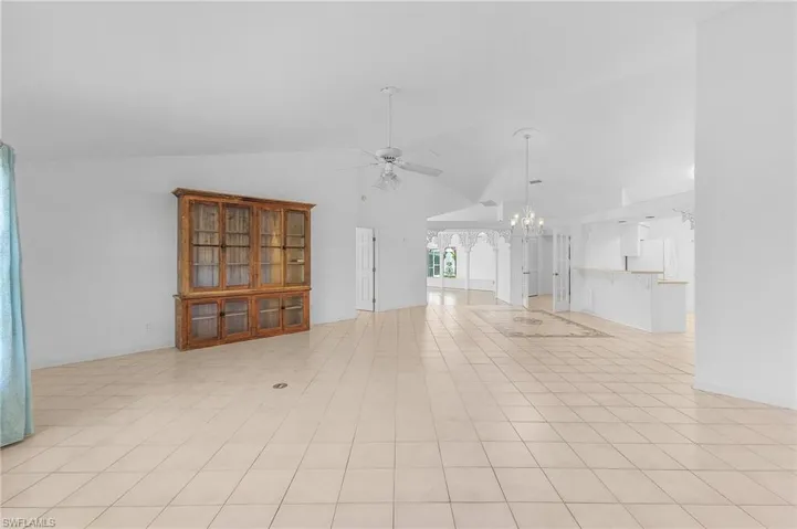 Unfurnished living room with ceiling fan with notable chandelier and vaulted ceiling