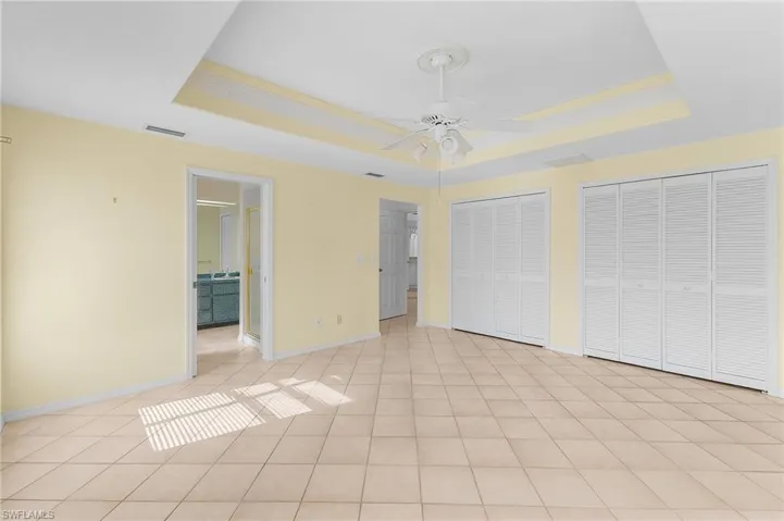 Unfurnished bedroom with light tile patterned floors, a tray ceiling, multiple closets, and ceiling fan