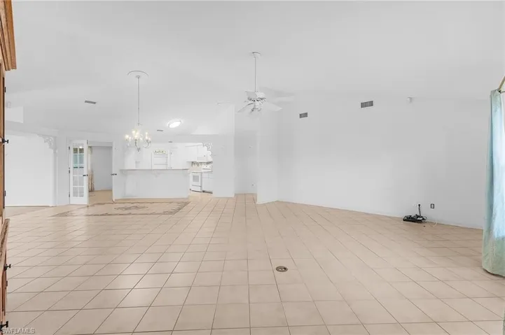 Unfurnished living room featuring ceiling fan with notable chandelier, high vaulted ceiling, and light tile patterned floors