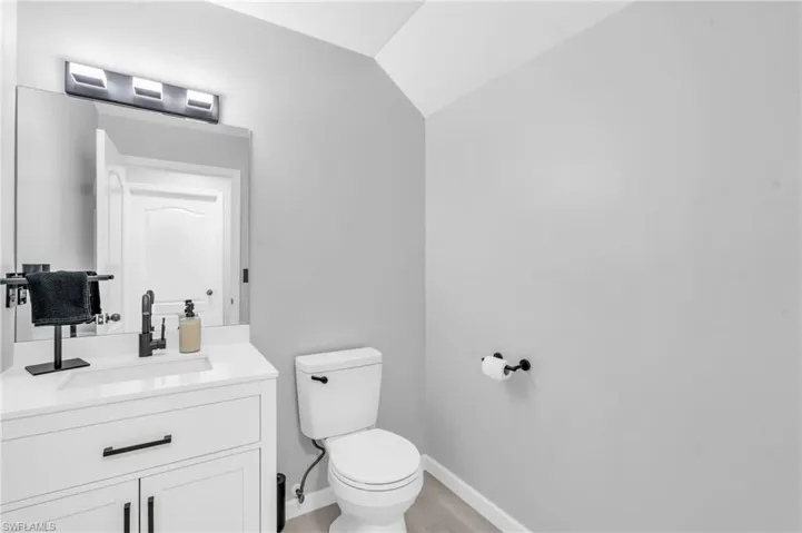 Bathroom with vanity, hardwood / wood-style floors, vaulted ceiling, and toilet