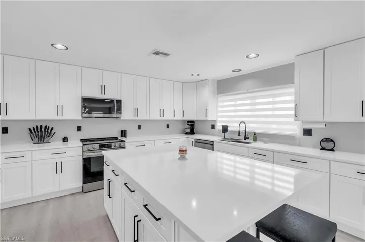 Kitchen with a kitchen island, a breakfast bar, sink, white cabinets, and stainless steel appliances
