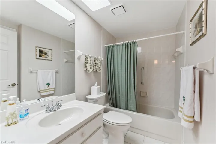 Bathroom featuring a skylight, toilet, shower / tub combo, vanity, and tile patterned flooring