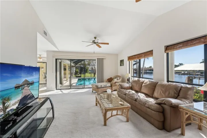 Living room featuring visible vents, light colored carpet, a sunroom, ceiling fan, and a water view