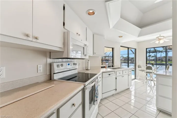 Kitchen featuring ceiling fan, light tile patterned floors, white appliances, white cabinetry, and light countertops