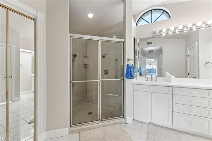 Full bath featuring tile patterned flooring, vanity, visible vents, vaulted ceiling, and a stall shower