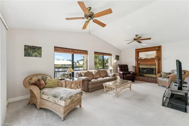 Living room featuring a ceiling fan, a glass covered fireplace, light carpet, and vaulted ceiling