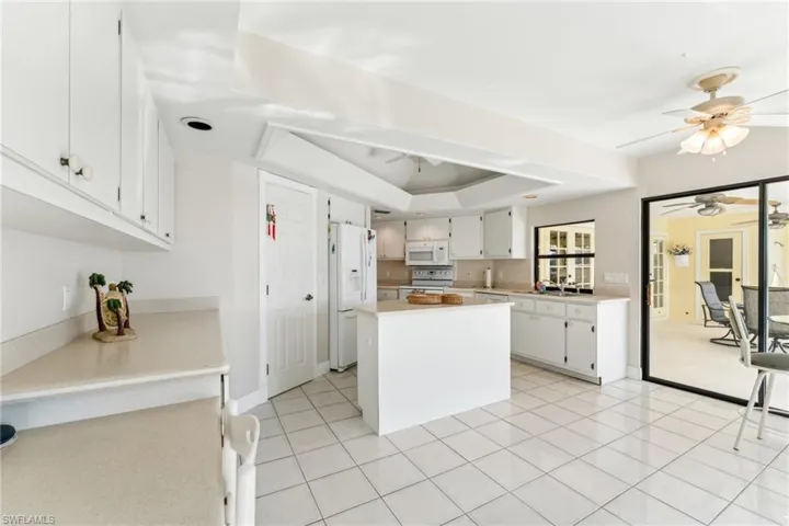 Kitchen with ceiling fan, white appliances, a sink, light countertops, and a raised ceiling