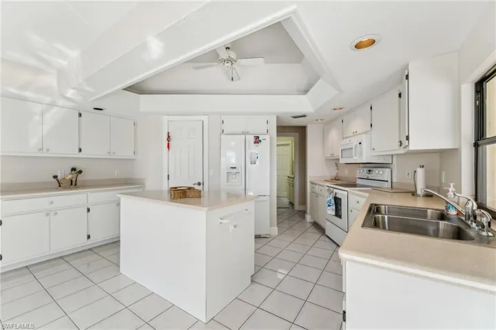 Kitchen featuring white appliances, white cabinets, a raised ceiling, a center island, and a sink