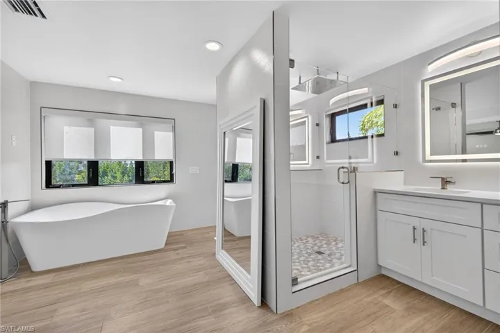 Dual door rainfall shower stall, modern soaking tub, designer tile, backlit mirrors, natural light.