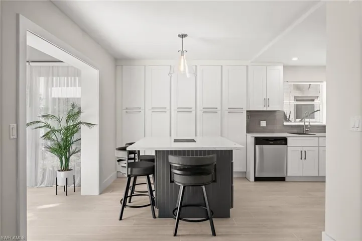 Kitchen featuring white cabinetry, a center island, stainless steel dishwasher, and a breakfast bar