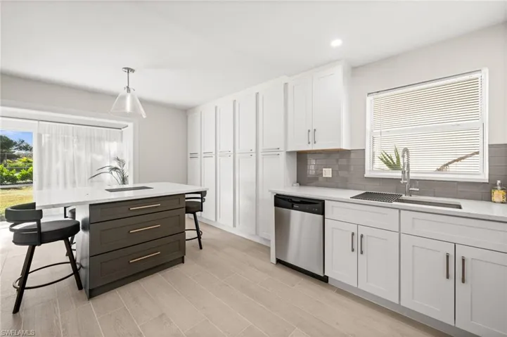 Kitchen featuring white cabinets, a kitchen breakfast bar, hanging light fixtures, dishwasher, and backsplash