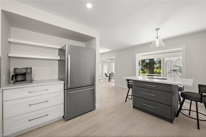 Kitchen featuring a breakfast bar, freestanding refrigerator, open shelves, hanging light fixtures, and light stone countertops