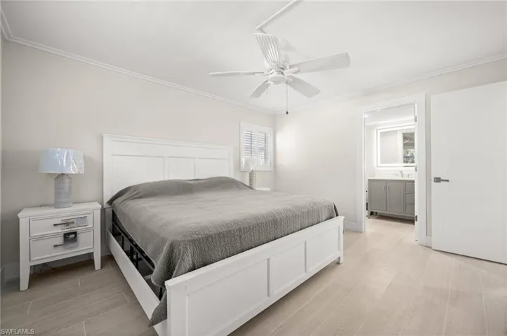 Bedroom with light wood-type flooring, ensuite bath, a ceiling fan, and ornamental molding