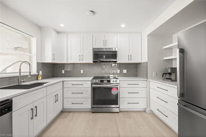 Kitchen with stainless steel appliances, white cabinets, open shelves, decorative backsplash, and light wood finished floors